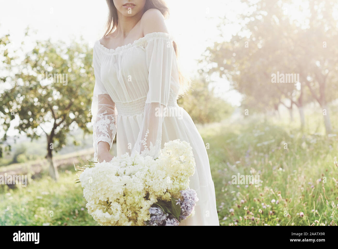 A beautiful young girl in a white light dress and a bouquet of summer ...
