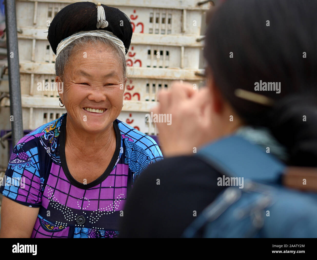 Japanese portrait photographer takes a photo of an elderly Thai H’mong saleswoman at Mae Sariang’s lively weekly Saturday market. Stock Photo