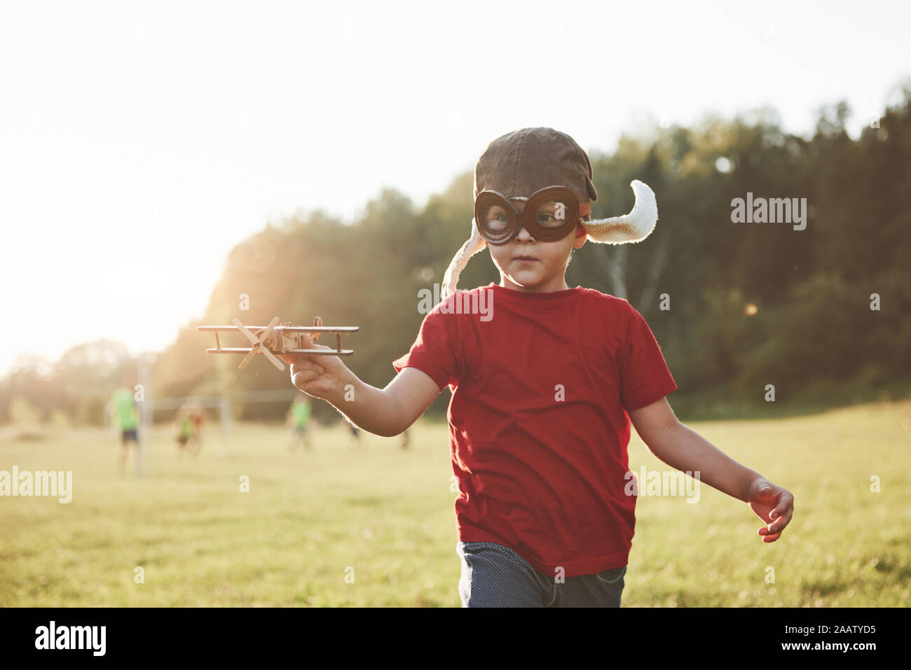 Happy kid in pilot helmet playing with a wooden toy airplane and ...