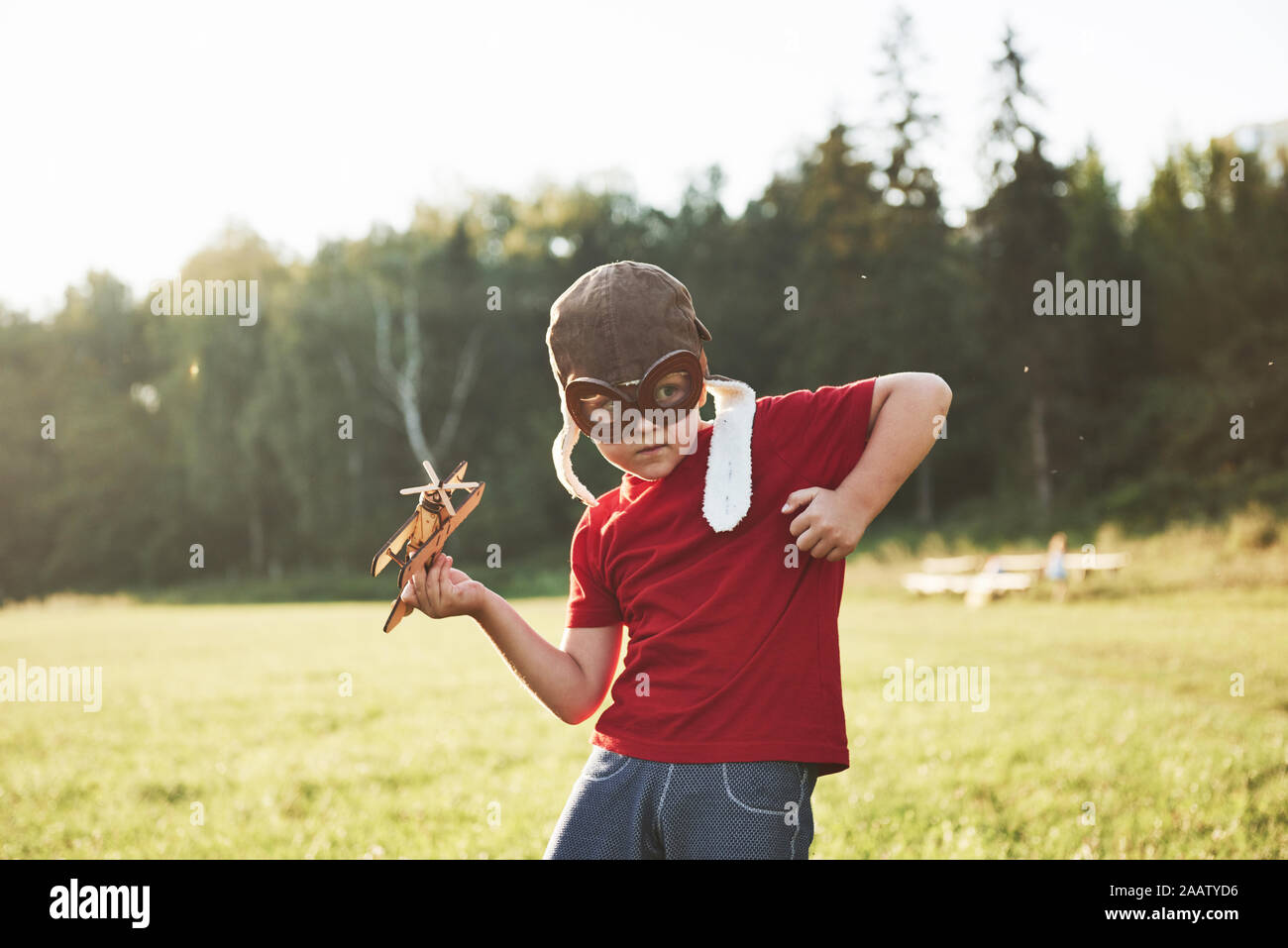 Happy kid in pilot helmet playing with a wooden toy airplane and ...