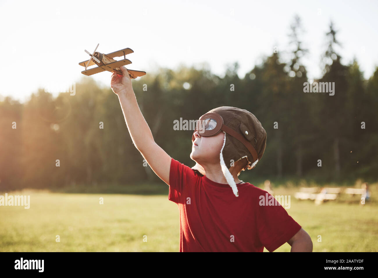 Happy kid in pilot helmet playing with a wooden toy airplane and ...
