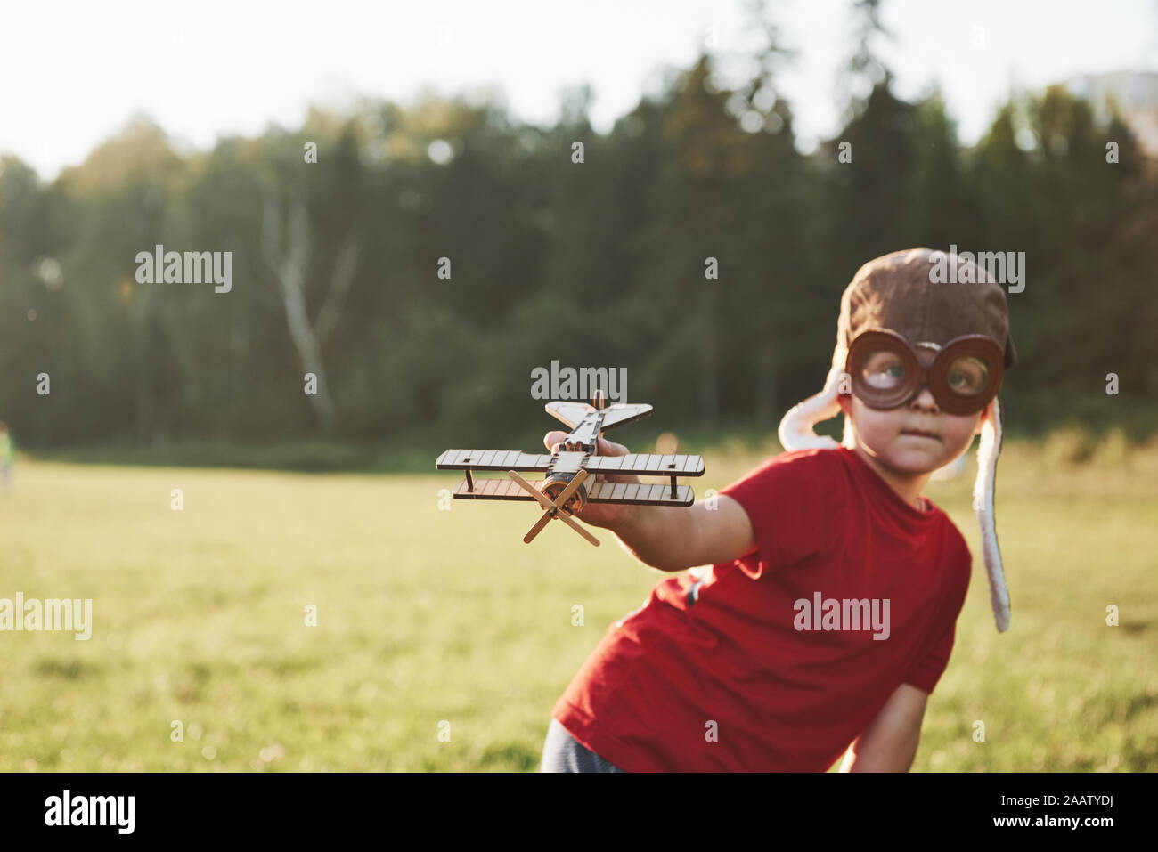Happy kid in pilot helmet playing with a wooden toy airplane and ...