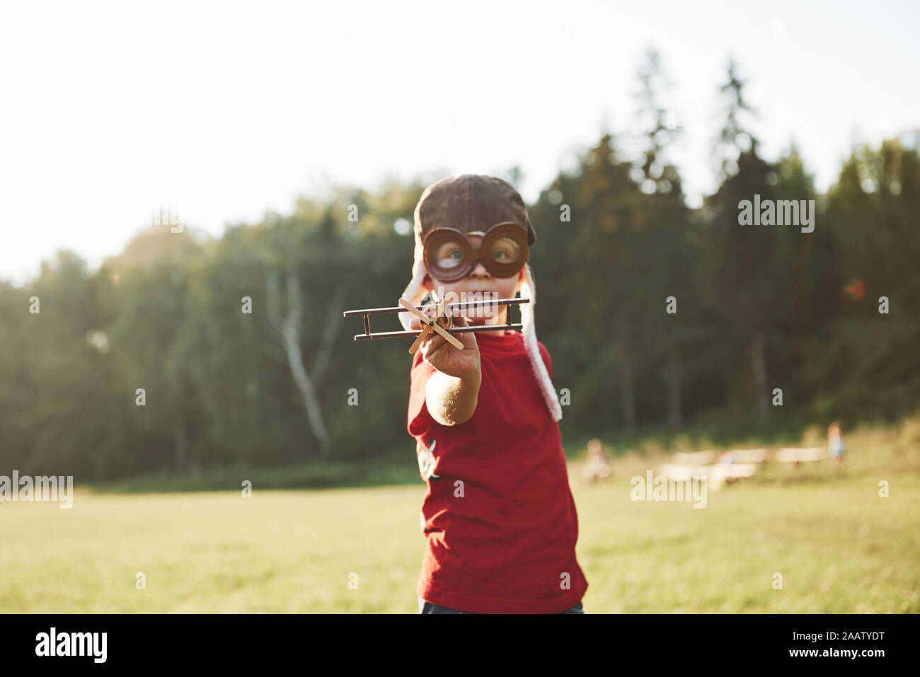 Happy kid in pilot helmet playing with a wooden toy airplane and ...