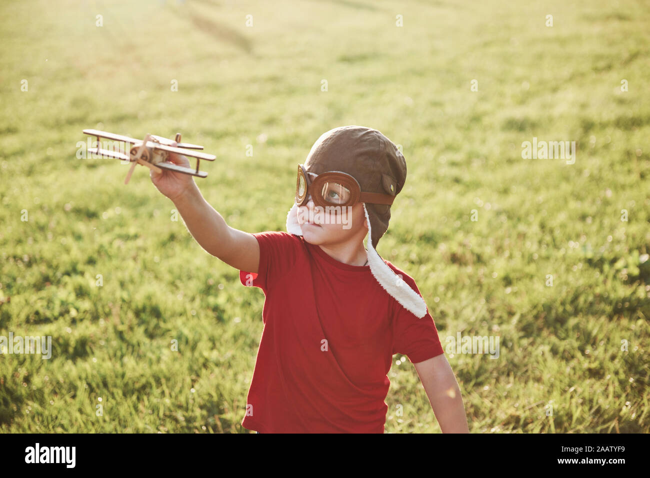 Happy kid in pilot helmet playing with a wooden toy airplane and ...