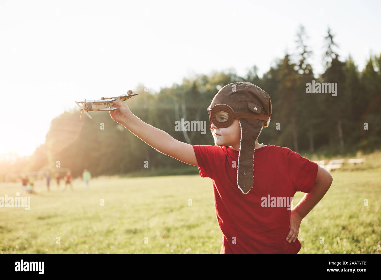 Happy kid in pilot helmet playing with a wooden toy airplane and ...