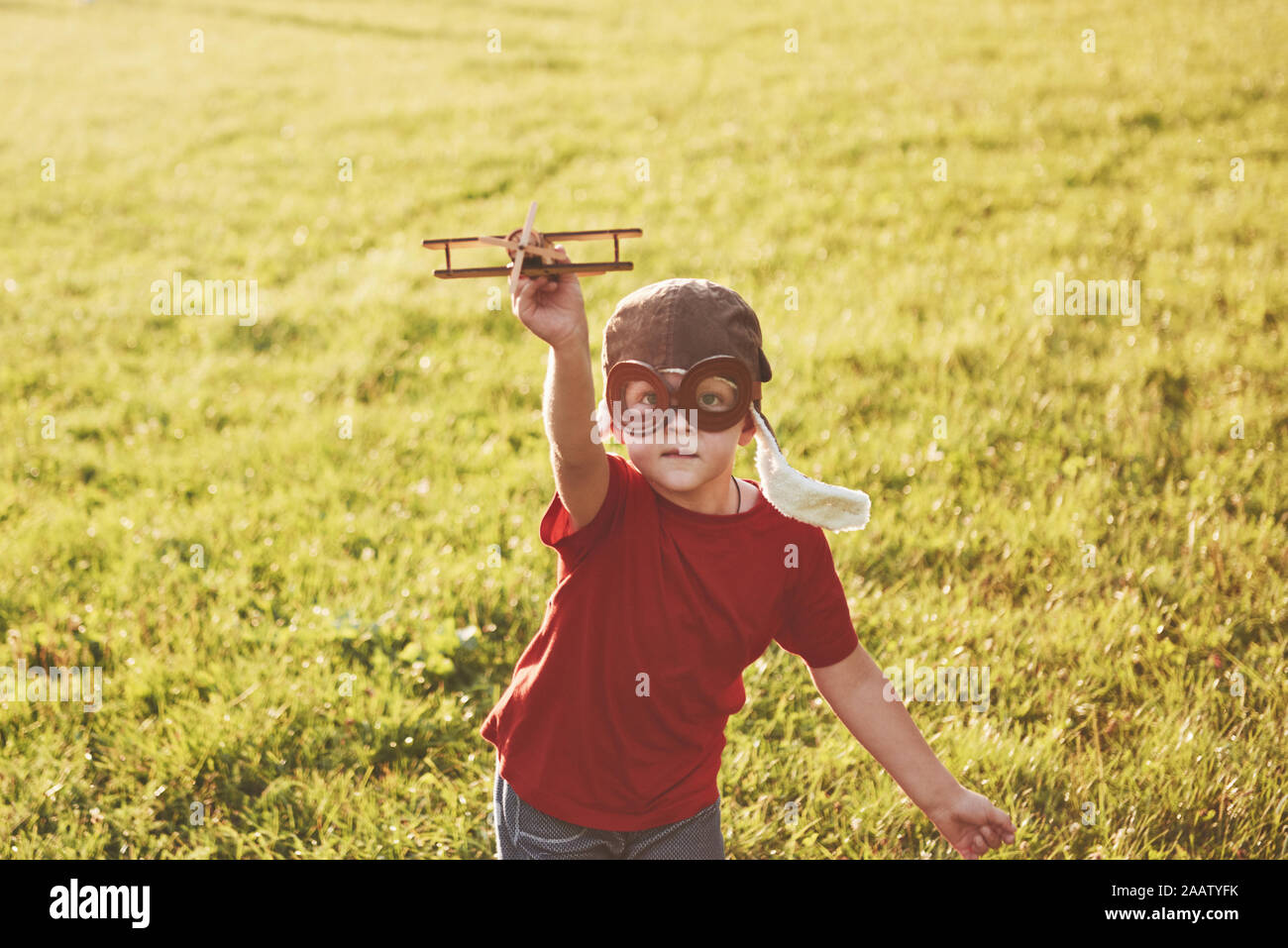 Happy kid in pilot helmet playing with a wooden toy airplane and ...