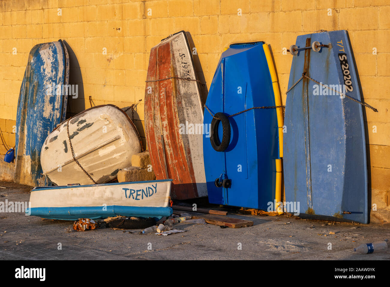 Small old boats, dingies left to dry, some stored vertically, secured with chain to a wall, Manoel Island quay in Malta Stock Photo