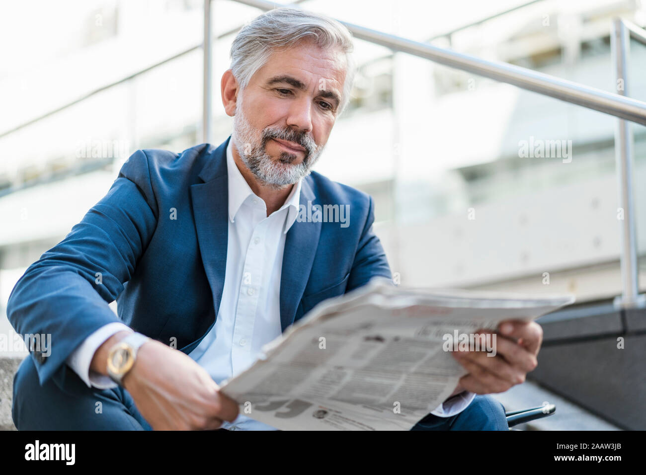 Mature businessman sitting on stairs in the city reading newspaper Stock Photo