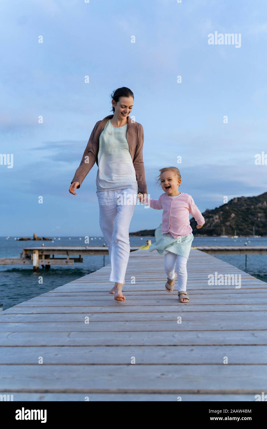 Happy mother with daughter walking on a jetty at sunset Stock Photo