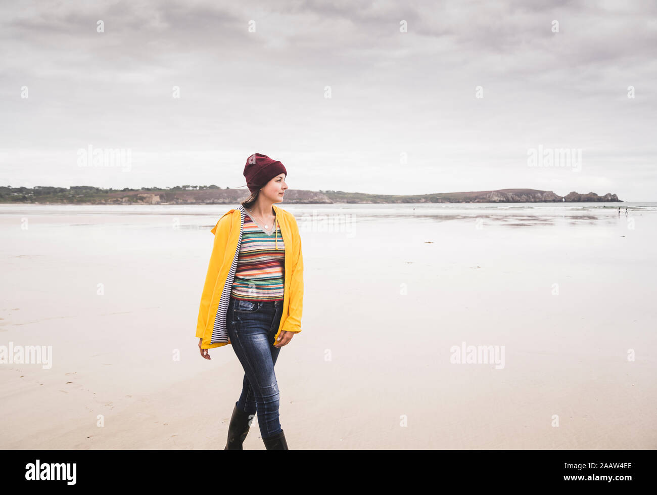 Young woman wearing yellow rain jacket at the beach, Bretagne, France Stock Photo