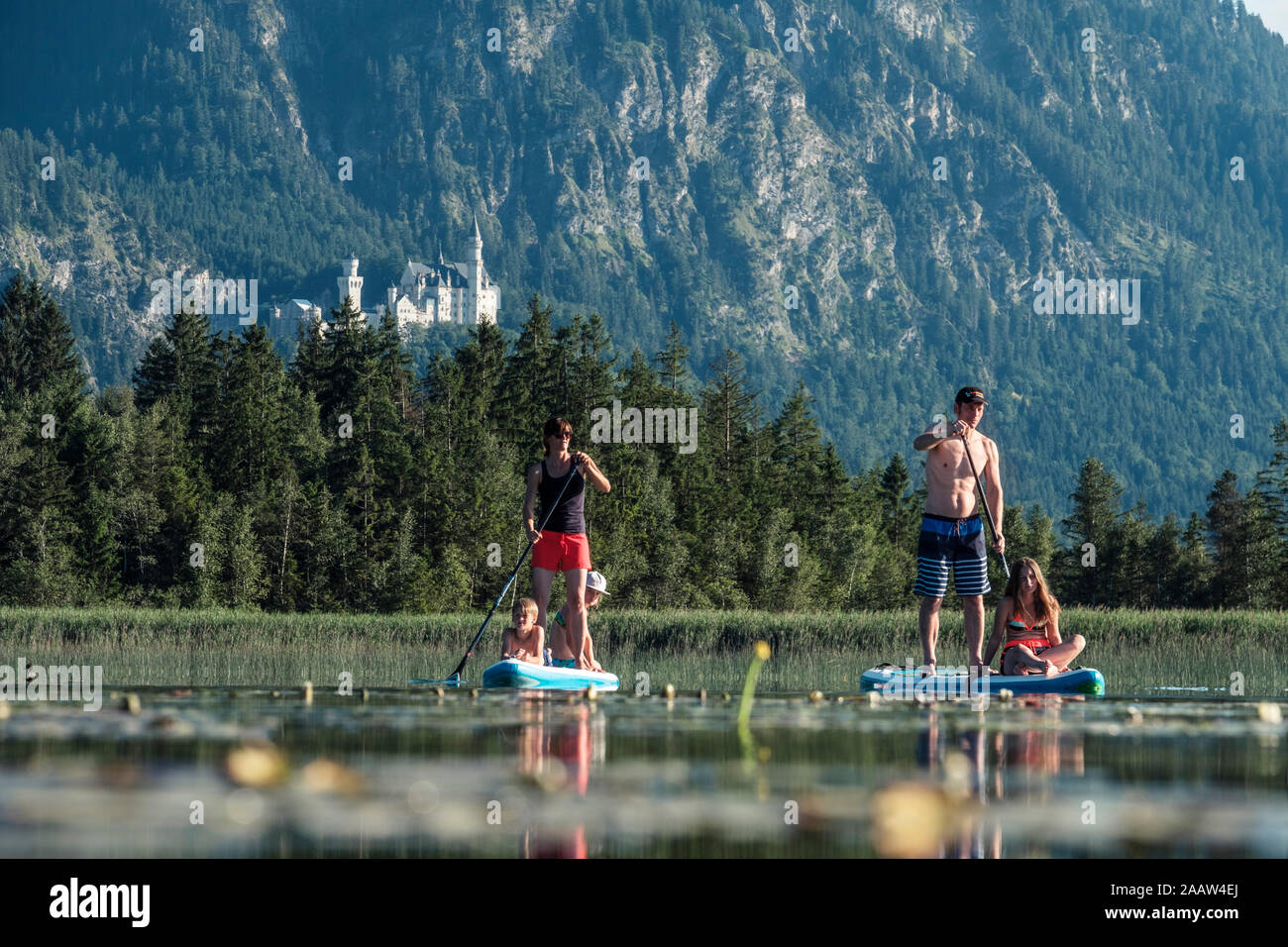 Family paddle boarding on lake Bannwaldsee, Castle Neuschwanstein in the background, Fuessen, Germany Stock Photo