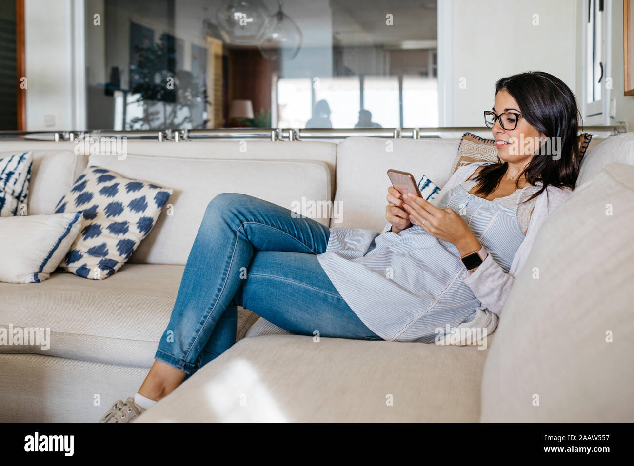 Smiling woman at home sitting on couch looking at cell phone Stock Photo