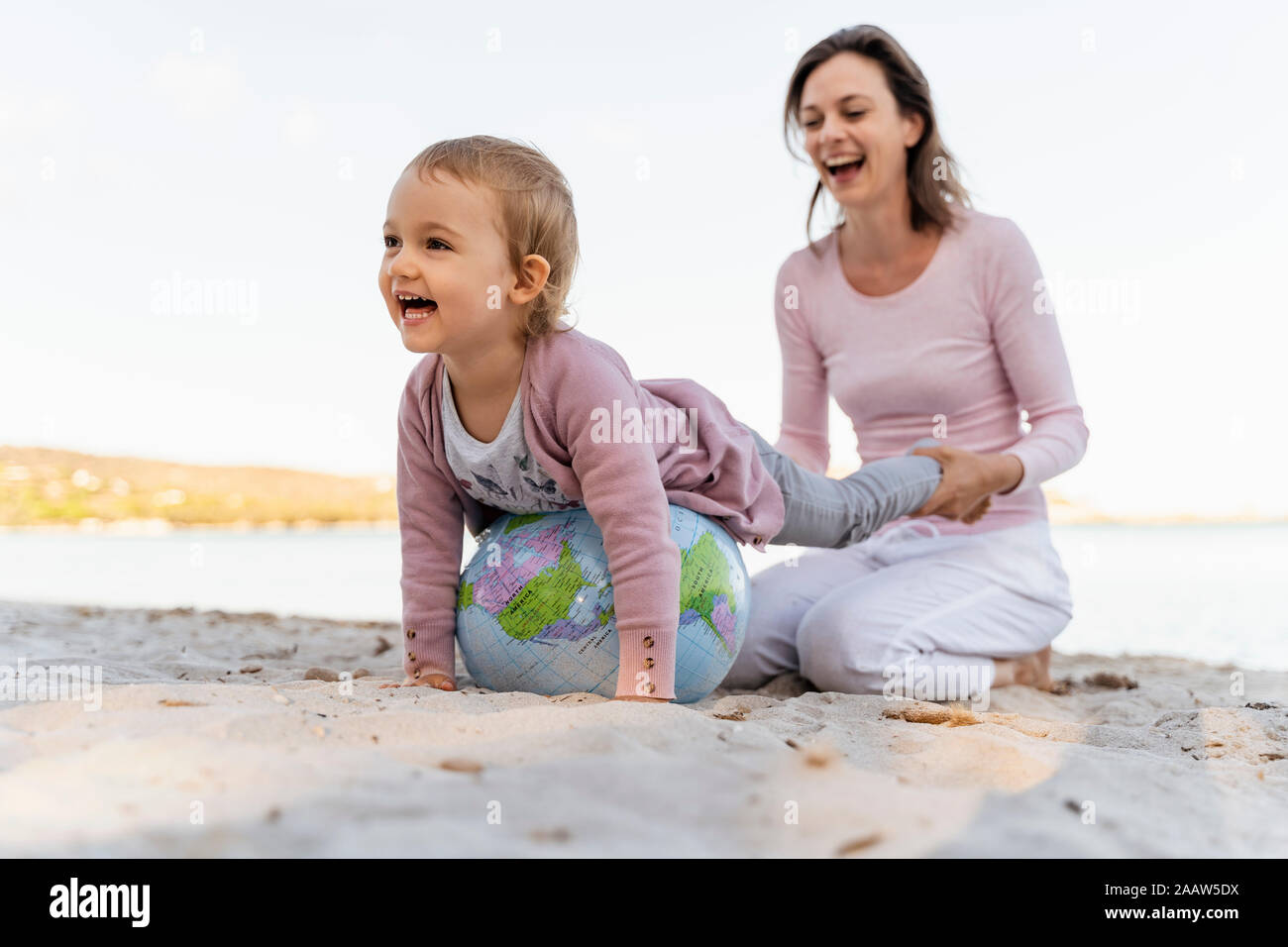 Mother and little daughter playing together with Earth beach ball at seashore Stock Photo