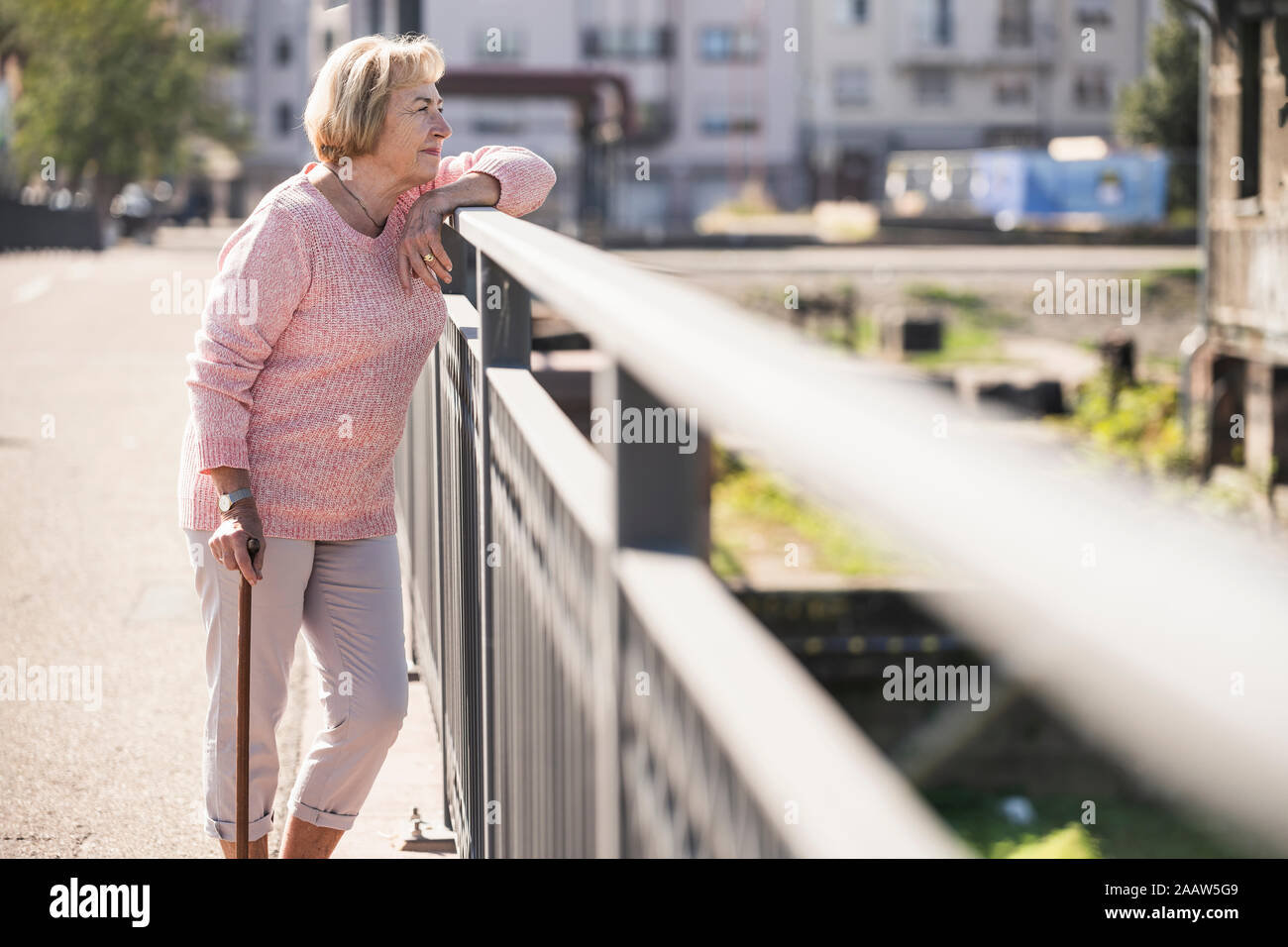 Senior woman walking on footbridge, using walking stick Stock Photo