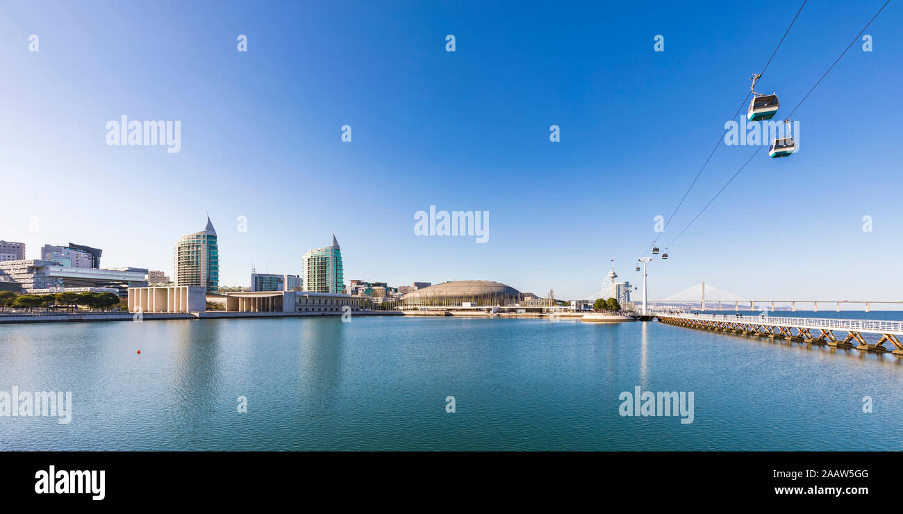 Overhead cable cars over Tagus River against blue sky in Lisbon, Portugal Stock Photo