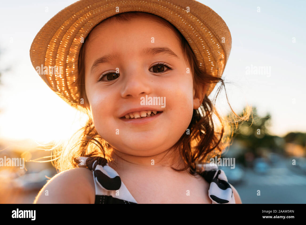 Portrait of smiling little girl wearing straw hat at sunset Stock Photo