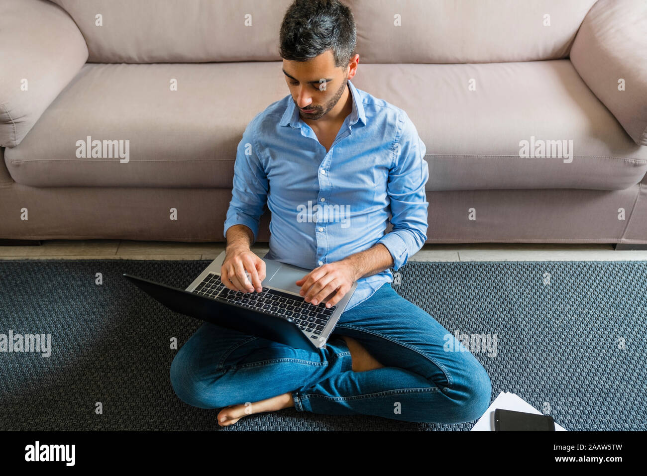 Young man sitting on the floor at home using laptop Stock Photo