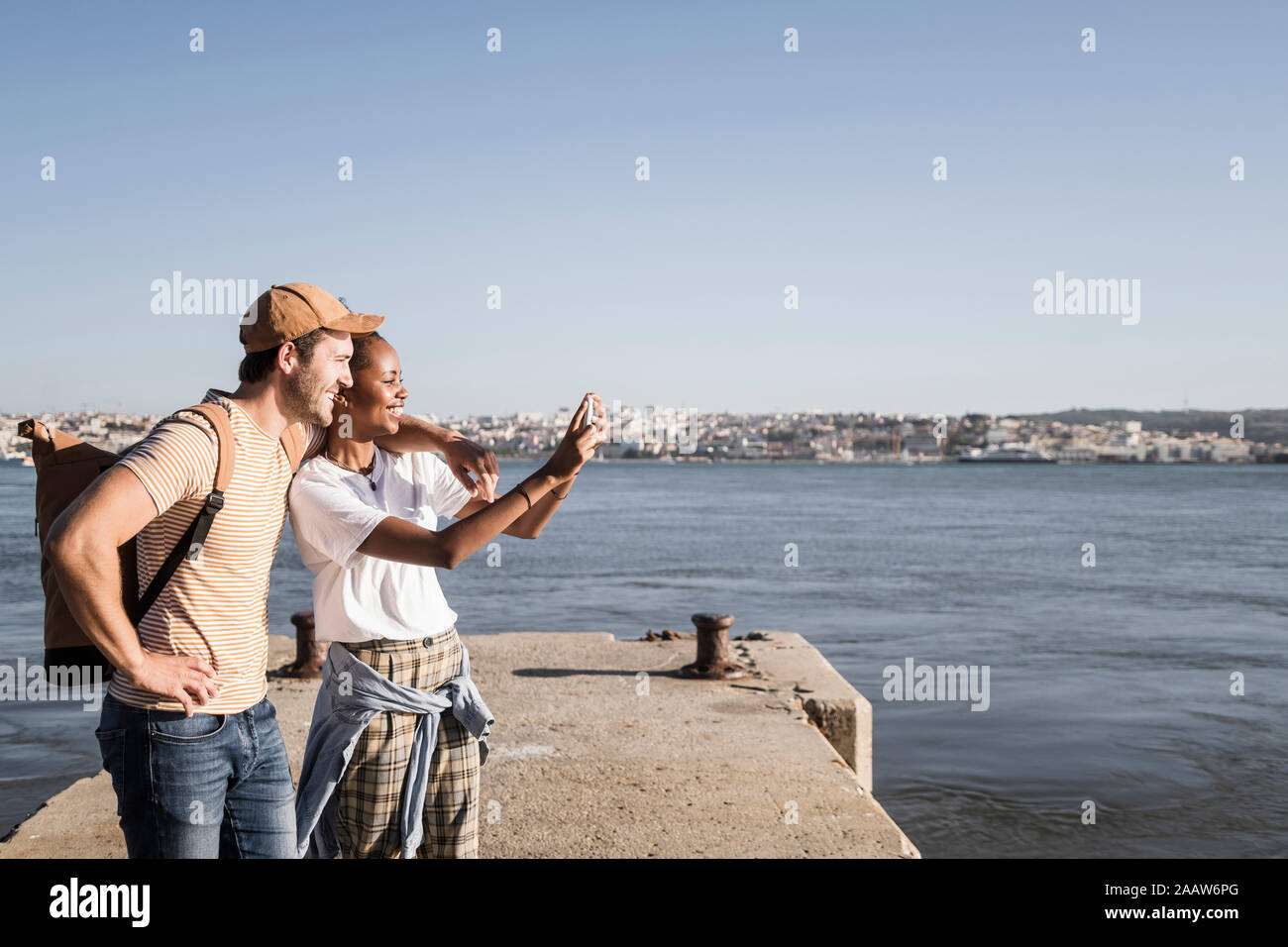 Happy young couple taking a selfie on pier at the waterfront, Lisbon, Portugal Stock Photo