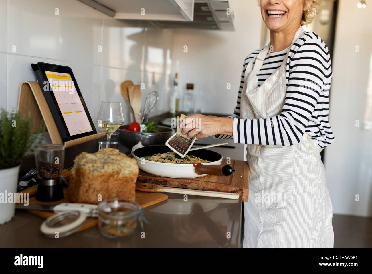 Happy mature woman with tablet cooking pasta dish in kitchen at home Stock Photo