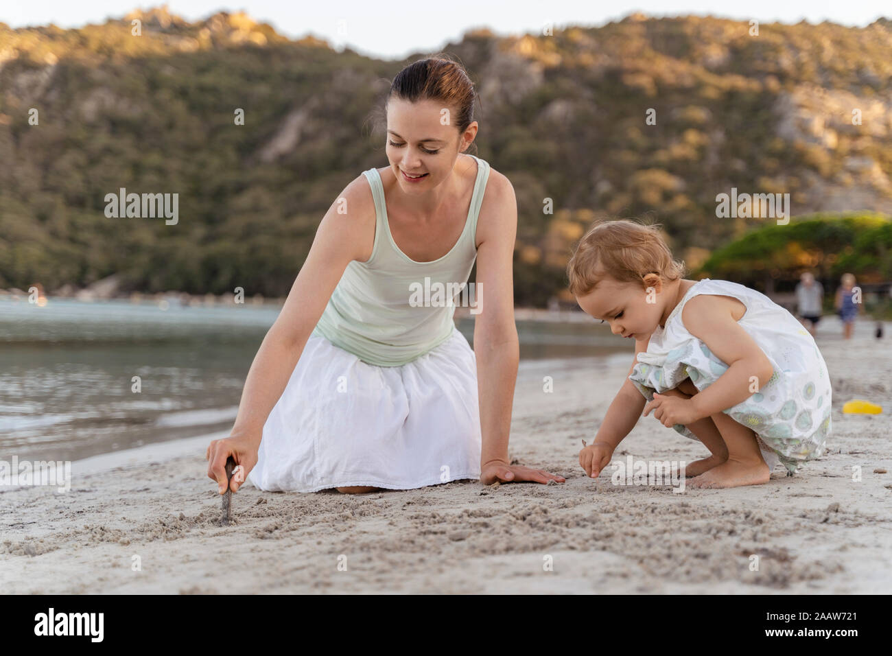 Mother and daughter drawing with little sticks in sand on the beach Stock Photo