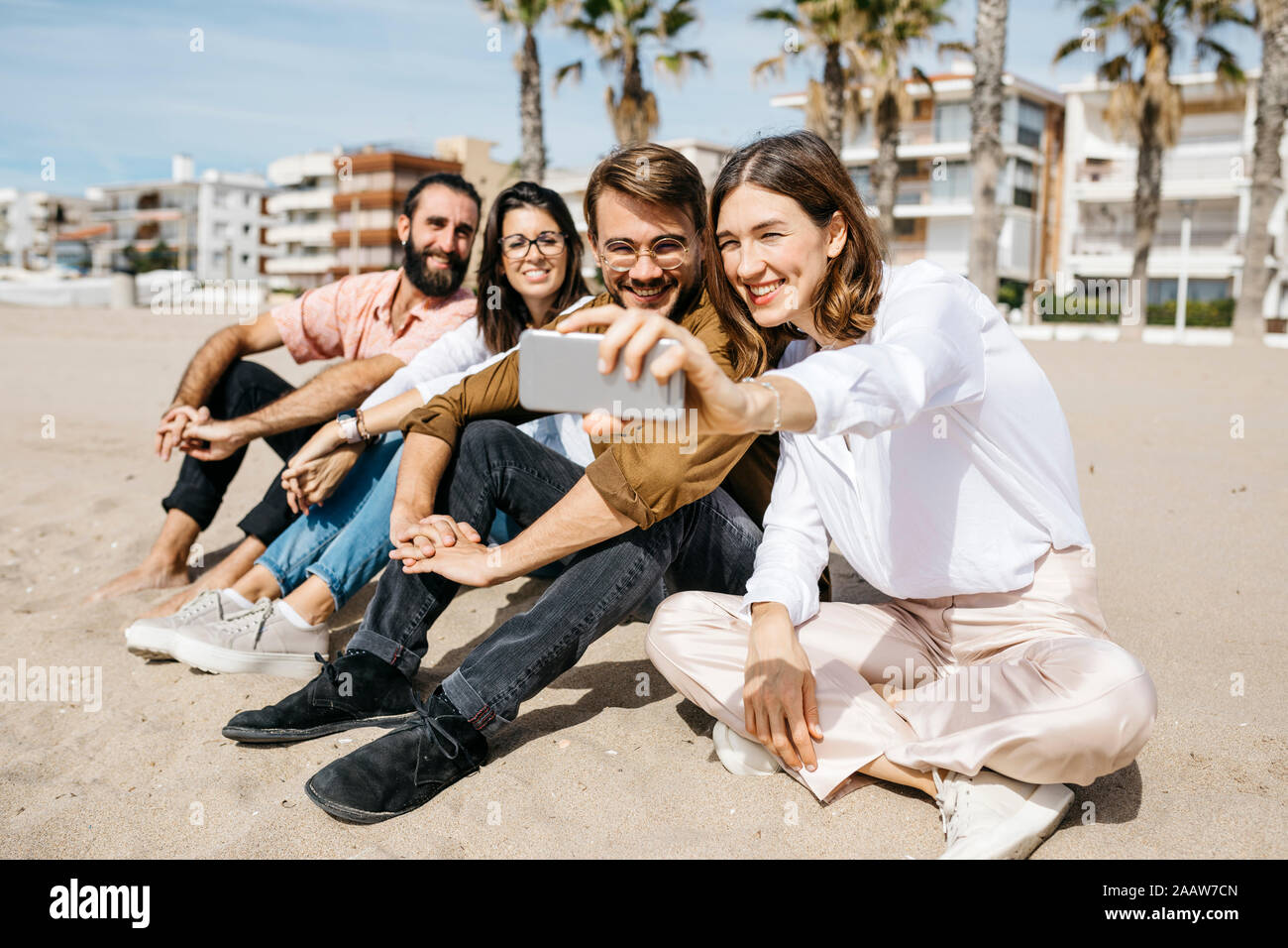 Happy friends sitting on the beach taking a selfie Stock Photo