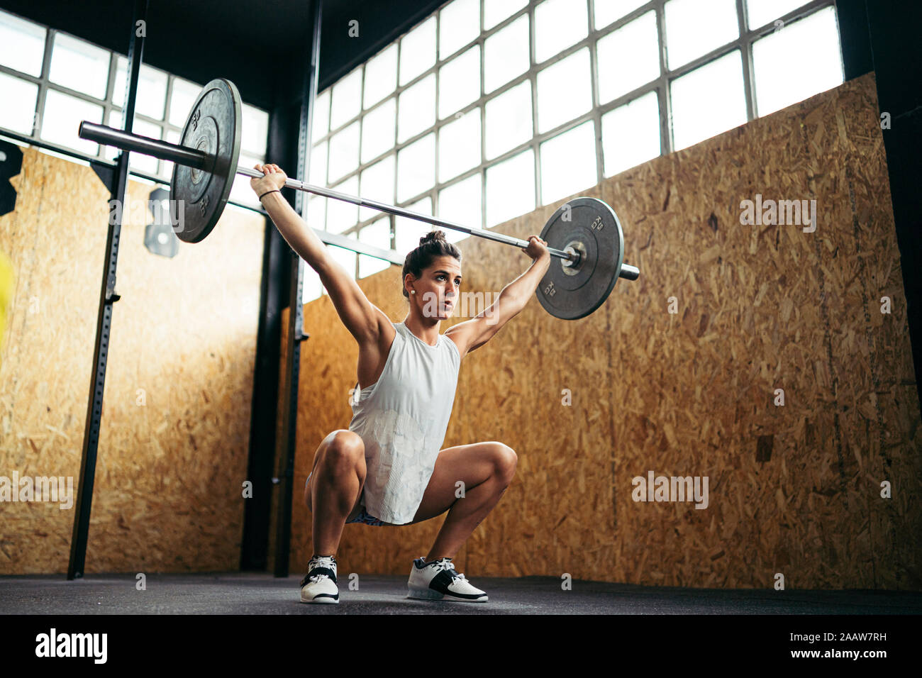 Young brunette woman doing overhead squat exercise at gym Stock Photo