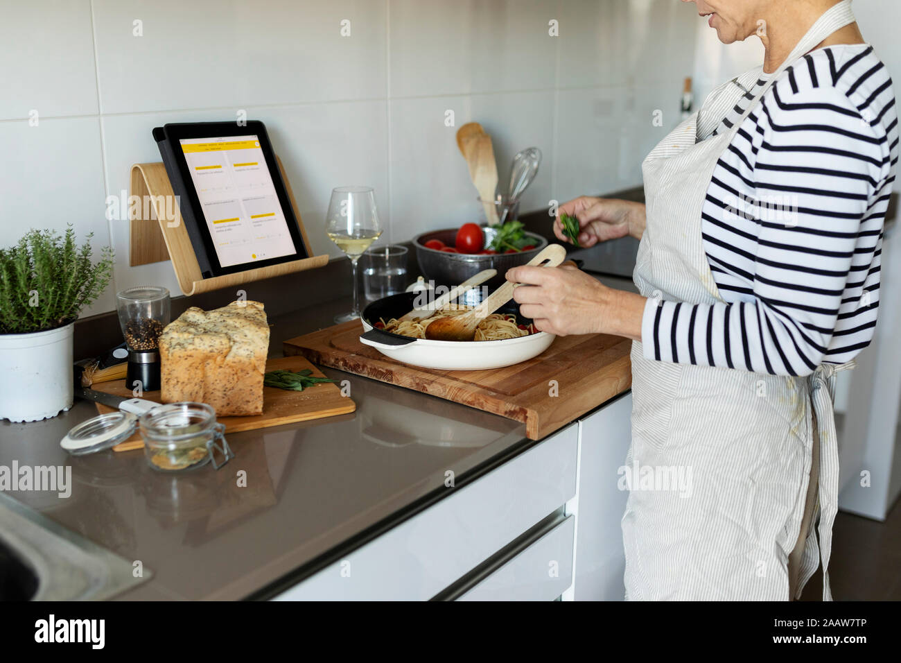 Close-up of woman with tablet cooking pasta dish in kitchen at home Stock Photo