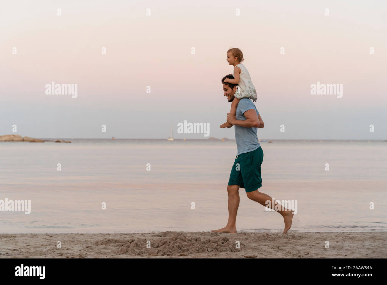 Happy father carrying daughter on shoulders on the beach at sunset Stock Photo