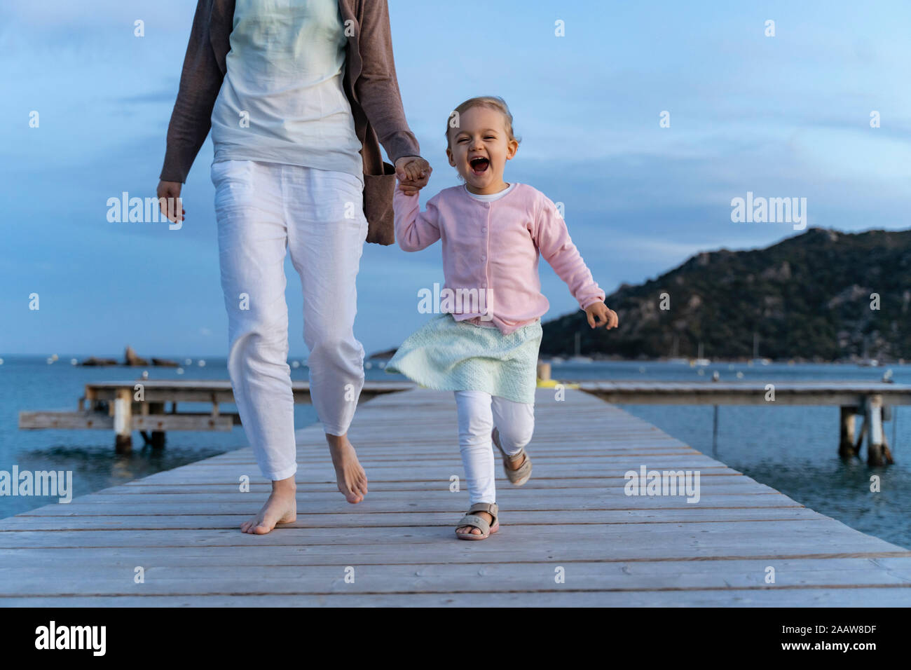 Happy girl walking with mother on a jetty at sunset Stock Photo