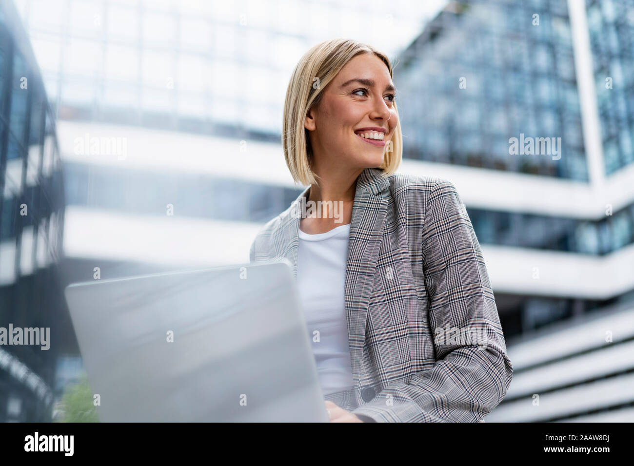 Smiling young businesswoman using laptop in the city Stock Photo