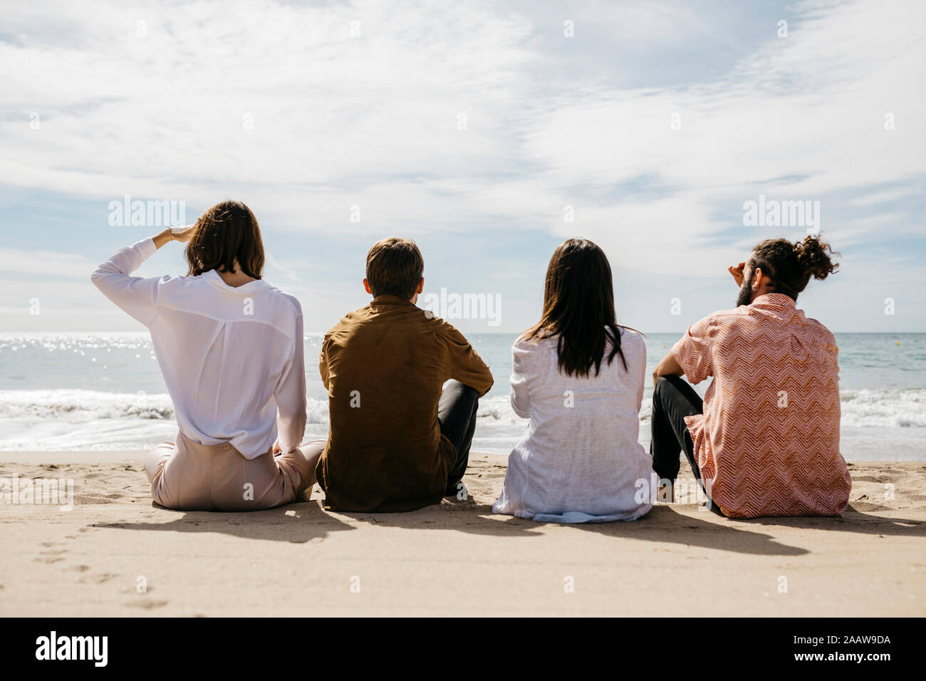Rear view of friends sitting on the beach looking at the sea Stock Photo