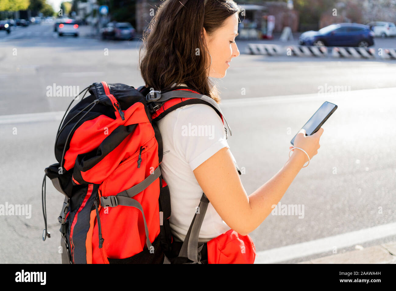 Young female backpacker with red backpack using smartphone in the city, Verona, Italy Stock Photo