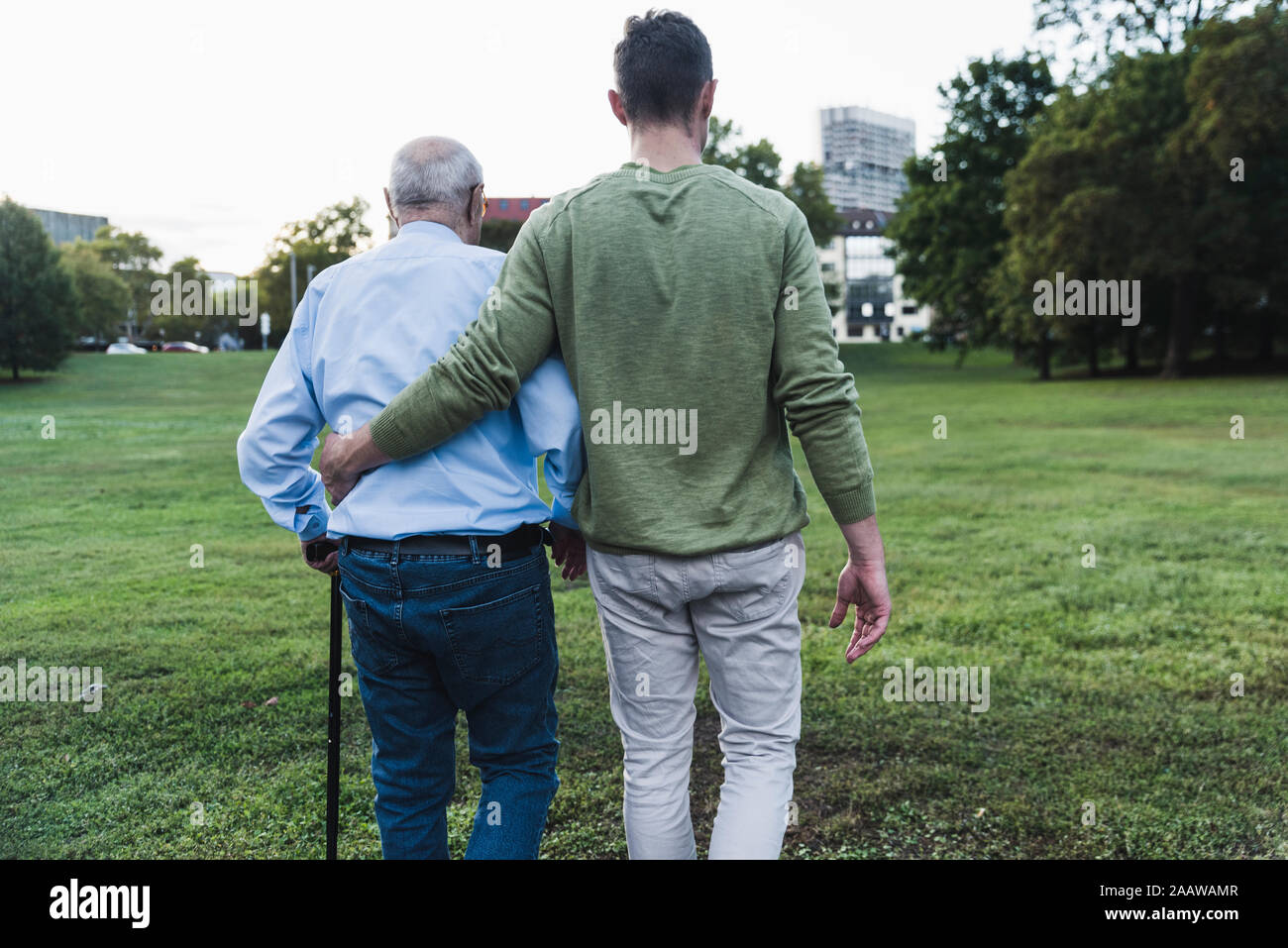 Back view of young man assisting his grandfather walking Stock Photo