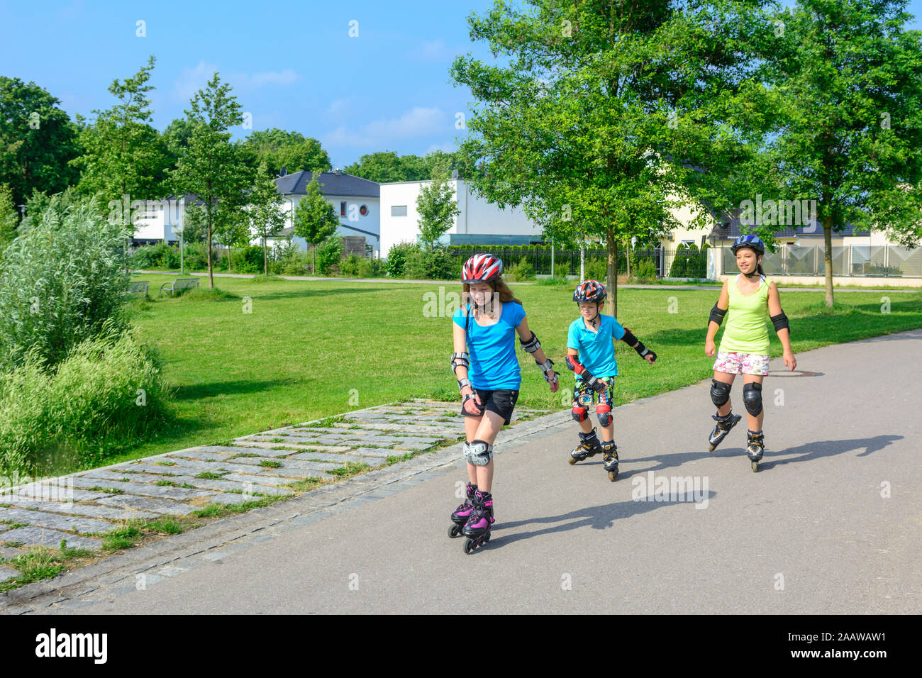 Young family doing a tour on inline skates in urban park at a sunny noon in summer Stock Photo