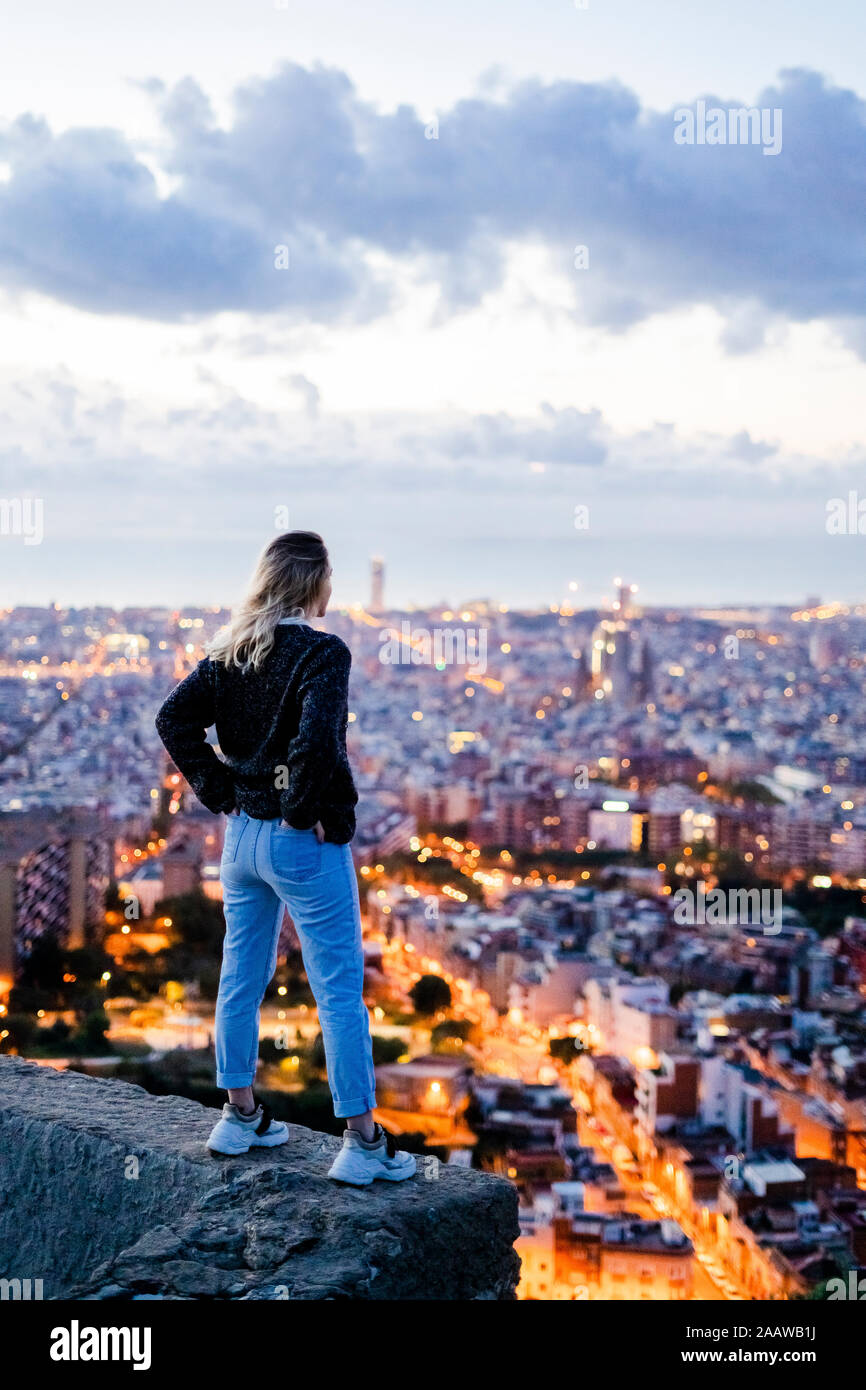 Rear view of young woman standing above the city at dawn, Barcelona, Spain Stock Photo