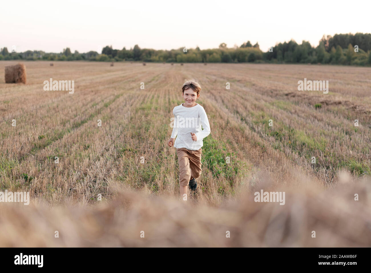 Smiling boy running over a stubble field Stock Photo