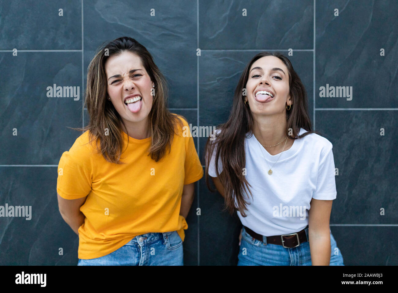 Two friends leaning on a wall and sticking out her tongues Stock Photo