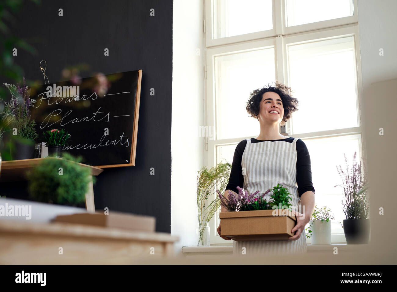 Happy young woman holding flowers in a cardboard box in a small shop Stock Photo