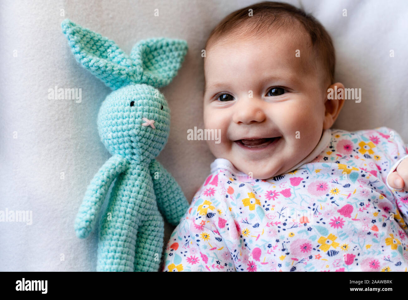 Baby girl with a stuffed bunny toy lying on bed Stock Photo