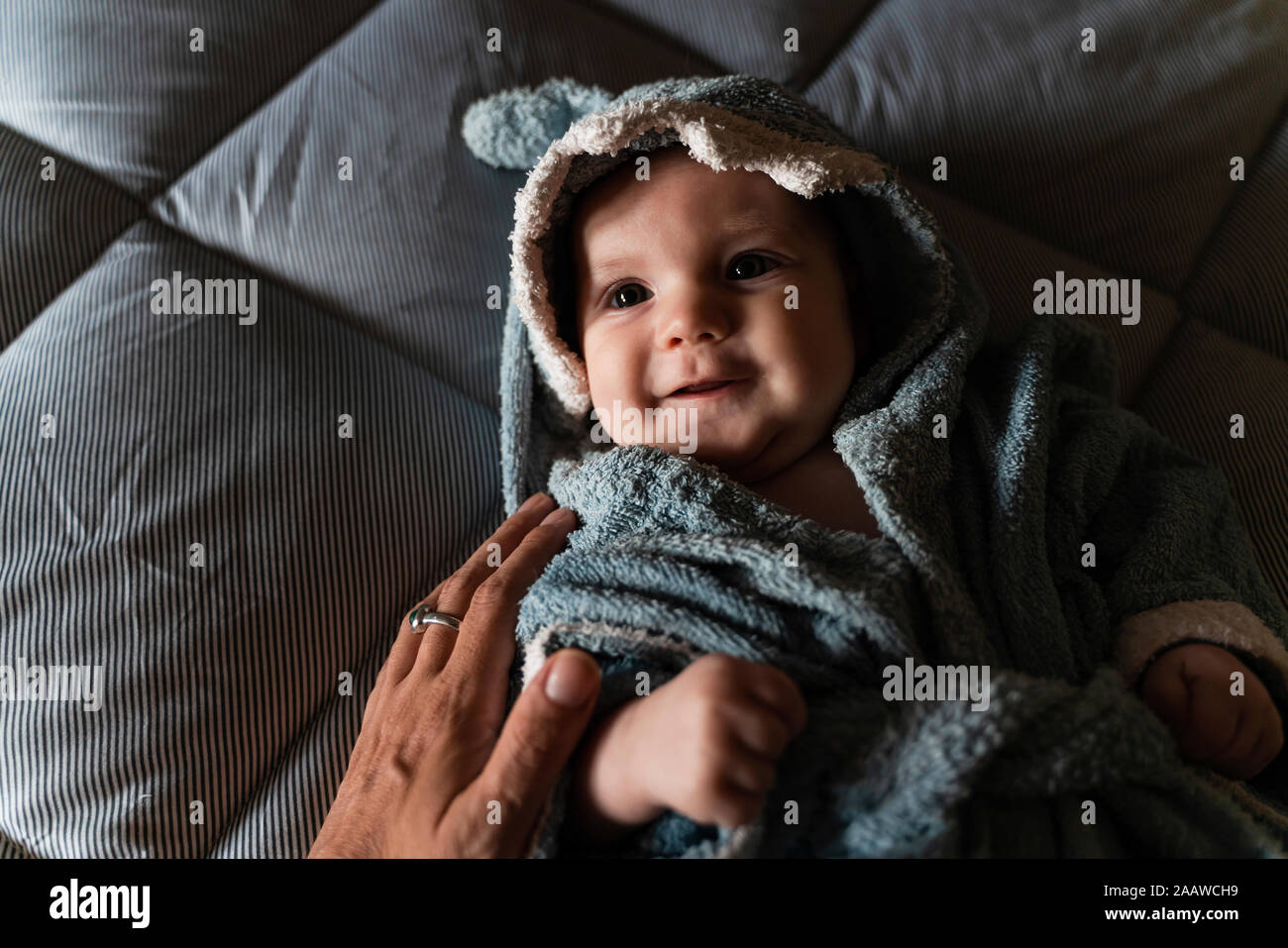 Portrait of baby girl lying on bed wrapped with shark shaped towel touched by mother's hand Stock Photo