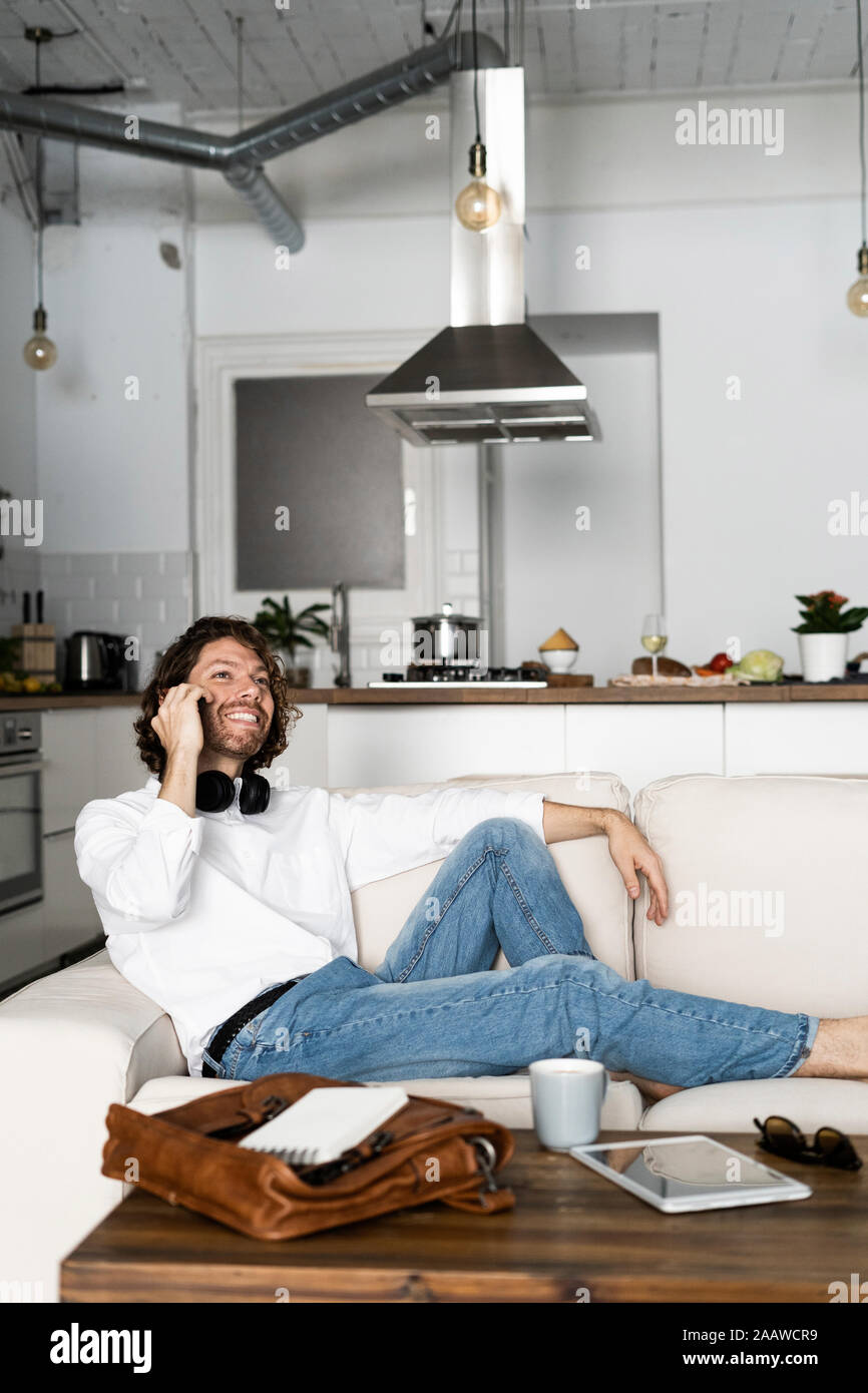 Relaxed man sitting on couch at home talking on the phone Stock Photo