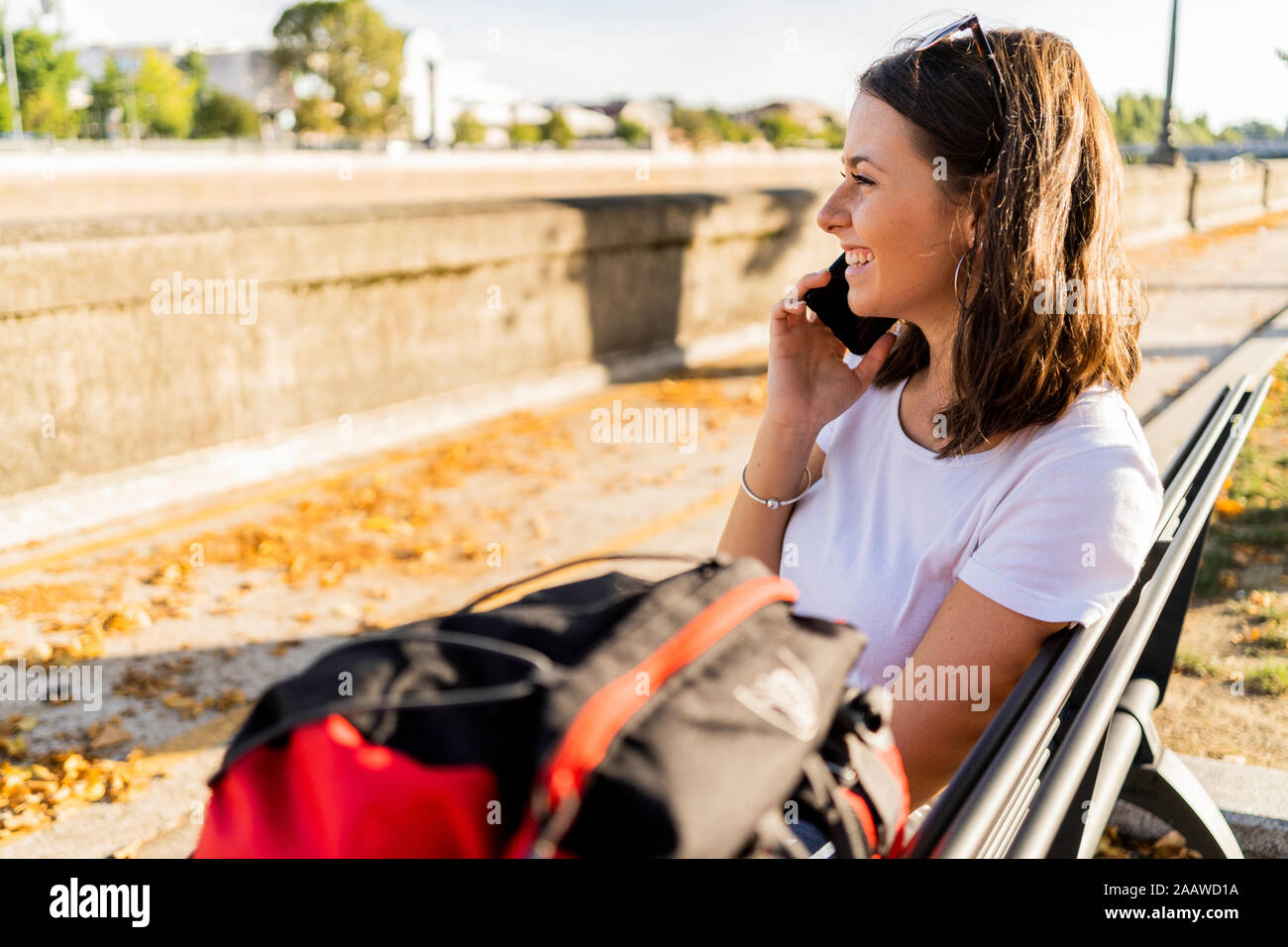 Young female backpacker with red backpack using smartphone, sitting on a benach in Verona, Italy Stock Photo