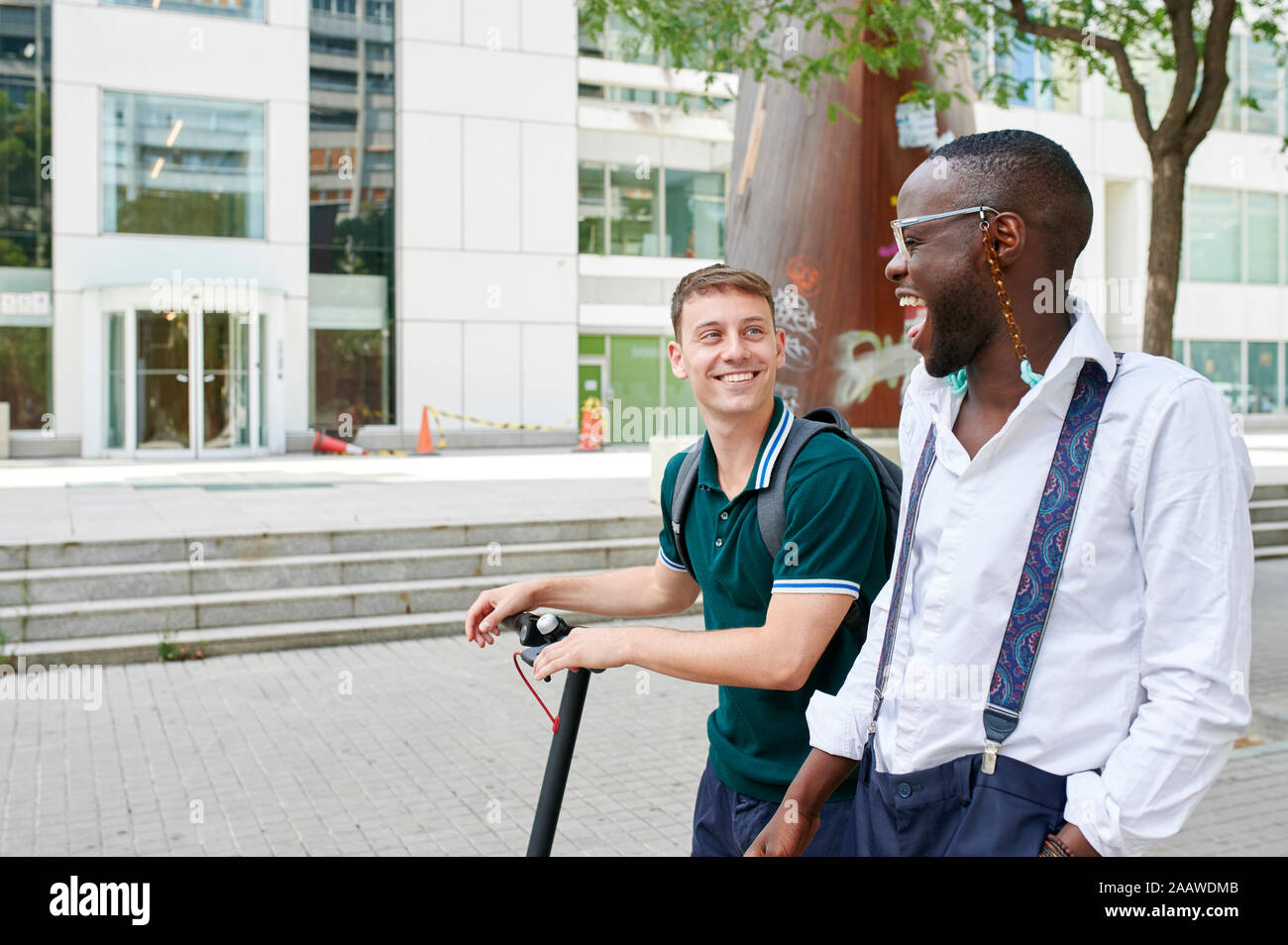 Two happy casual businessmen with e-scooter talking in the city Stock Photo