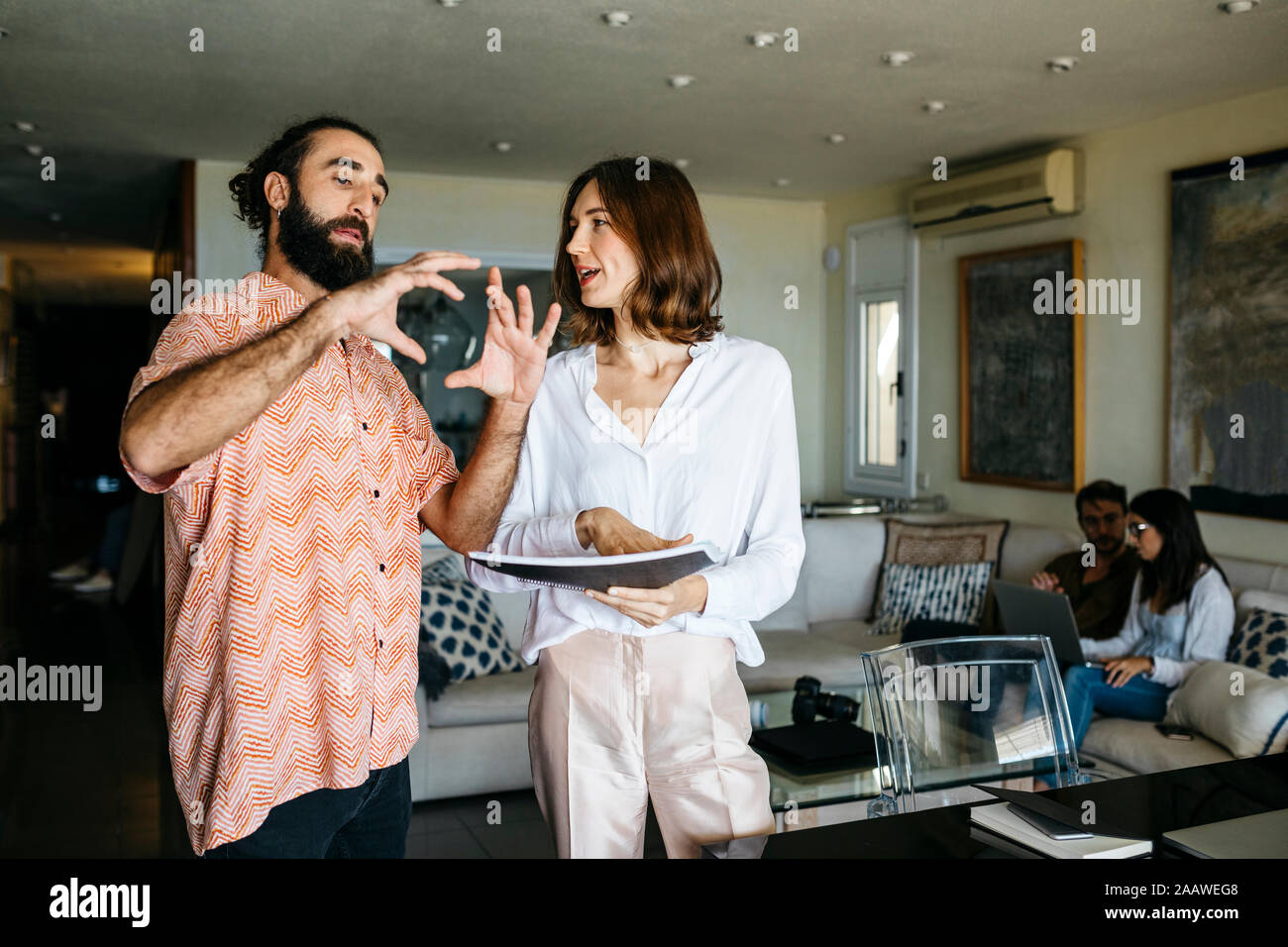 Man and woman talking with friends sitting on couch in background Stock Photo