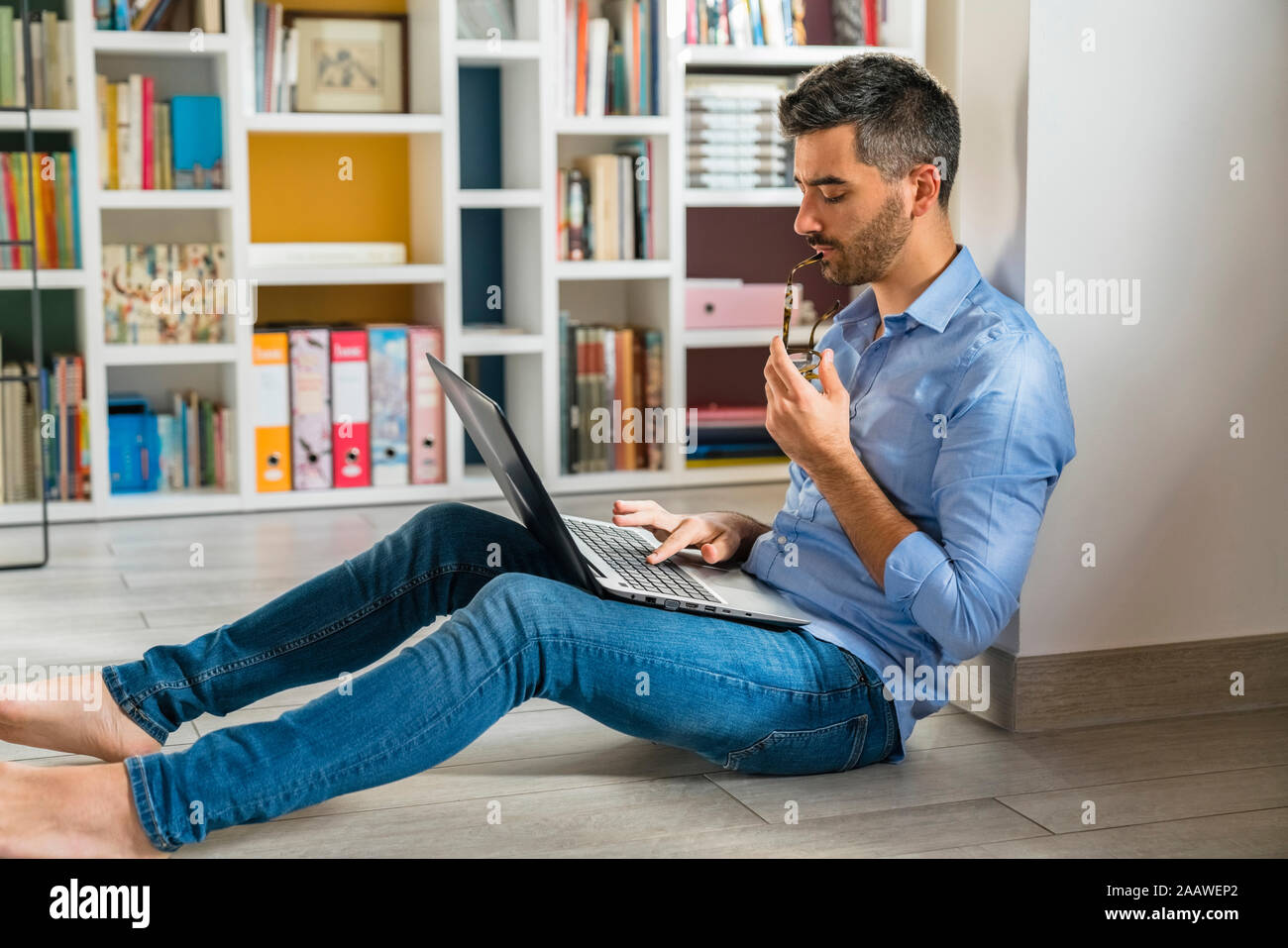 Young man sitting on the floor at home using laptop Stock Photo