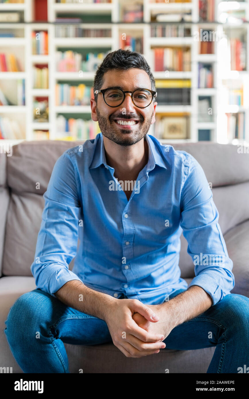 Portrait of happy young man sitting on the couch at home Stock Photo