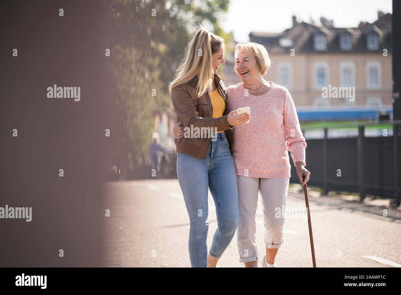 Granddaughter and her grandmother walking on footbridge and using smartphone Stock Photo