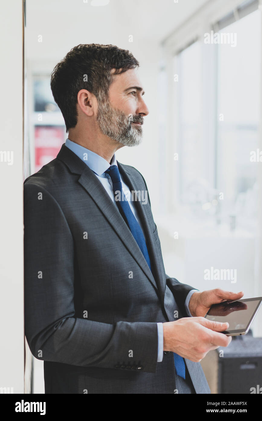 Mature businessman with tablet in office looking out of window Stock Photo