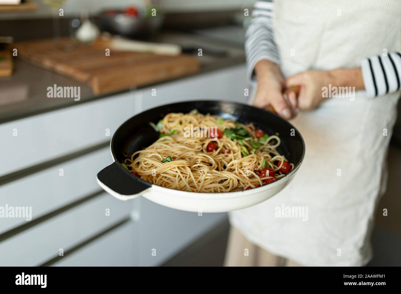 Close-up of woman holding a pan with pasta dish in kitchen at home Stock Photo