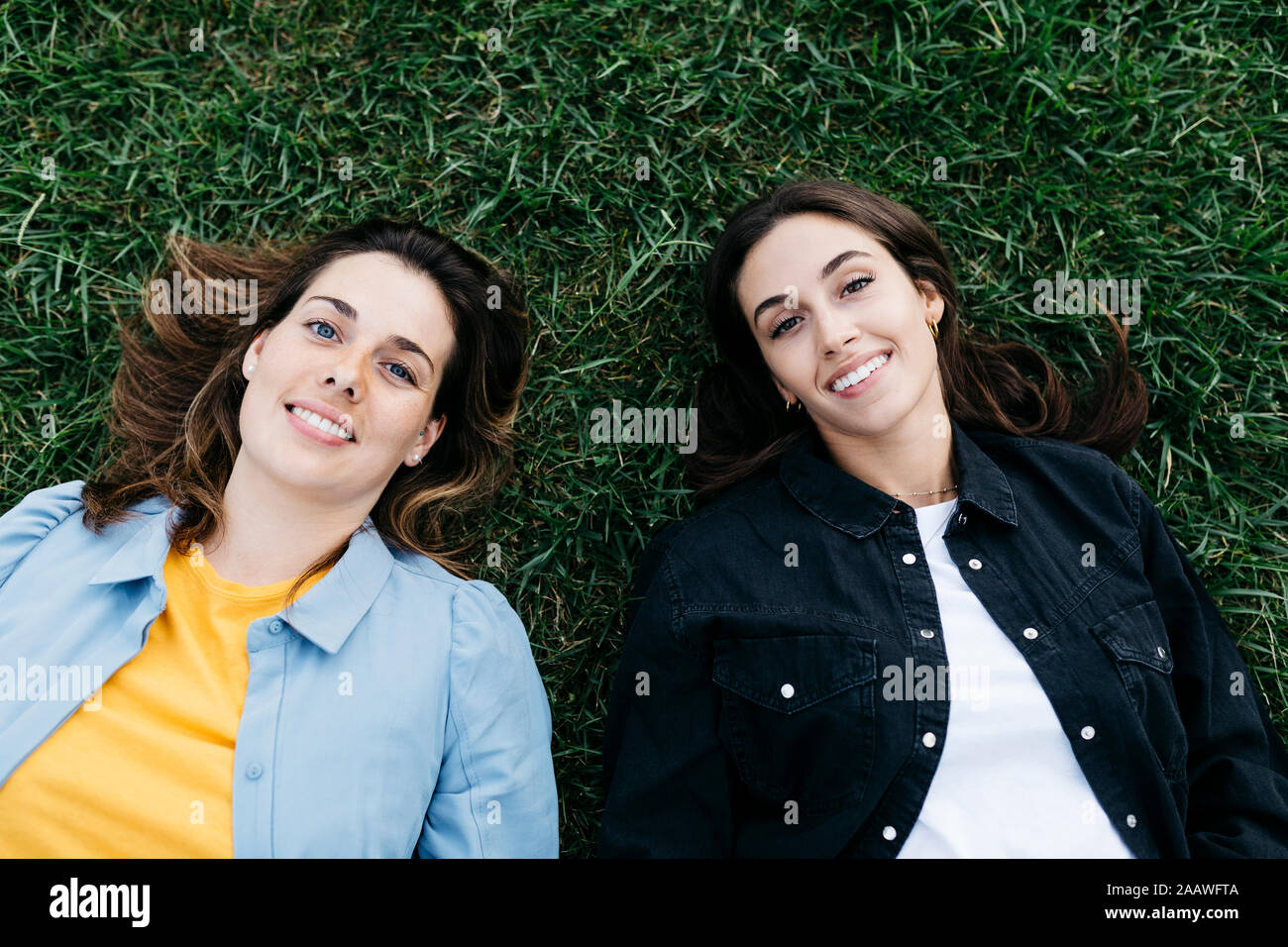 Portrait of two friends looking at camera, lying on the grass Stock Photo